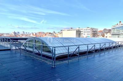 Façade vitrée d'un bâtiment moderne avec une terrasse en bois éclairée par le soleil.