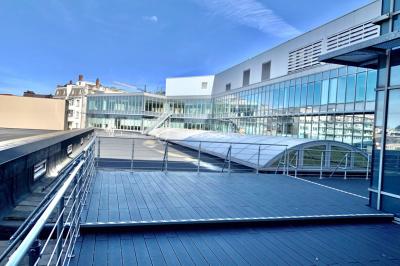 Façade vitrée d'un bâtiment moderne avec une terrasse en bois éclairée par le soleil.