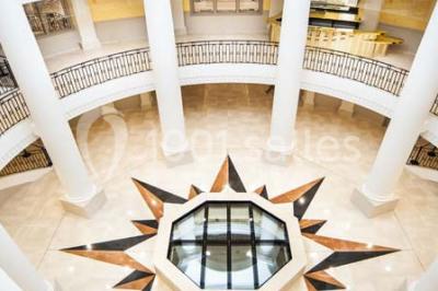 Salle spacieuse avec parquet en bois clair, colonnes blanches, plafonds ondulés et luminaires suspendus.