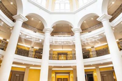 Salle spacieuse avec parquet en bois clair, colonnes blanches, plafonds ondulés et luminaires suspendus.