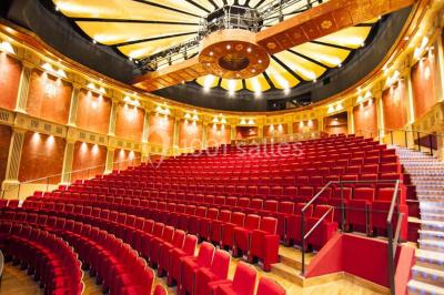 Salle spacieuse avec parquet en bois clair, colonnes blanches, plafonds ondulés et luminaires suspendus.