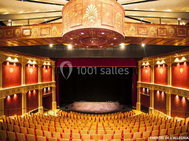 Salle de théâtre avec sièges rouges, scène centrale et plafond orné d'un lustre décoratif.