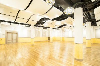 Salle spacieuse avec parquet en bois clair, colonnes blanches, plafonds ondulés et luminaires suspendus.