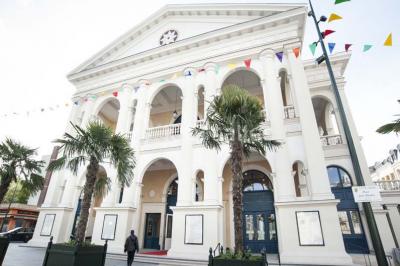 Salle de conférence lumineuse avec des rangées de chaises blanches et une table en bois au premier plan.