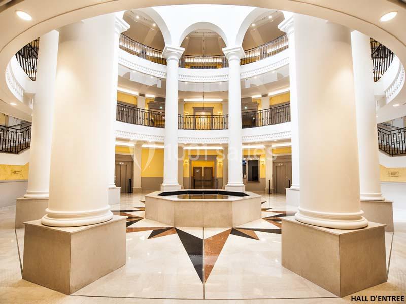 Hall d'entrée spacieux avec colonnes blanches, sol en marbre et puits de lumière central.