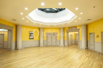 Salle de conférence lumineuse avec des rangées de chaises blanches et une table en bois au premier plan.