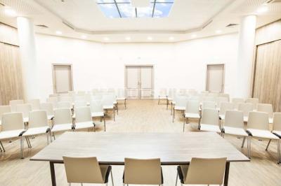 Salle de conférence lumineuse avec des rangées de chaises blanches et une table en bois au premier plan.