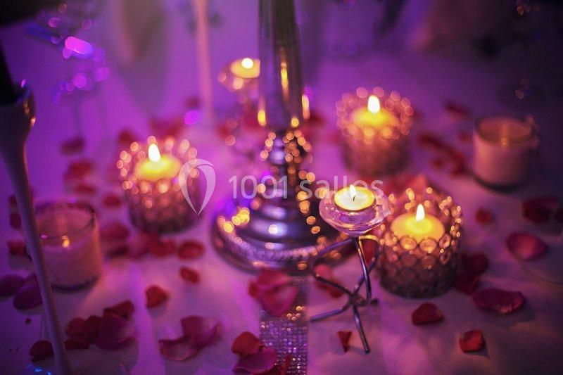 Bougies allumées entourées de pétales de rose sur une table décorée dans une ambiance tamisée et romantique.