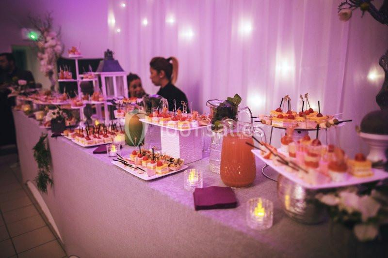 Buffet décoré avec des verrines, amuse-bouches et boissons, éclairé par une lumière tamisée dans une ambiance festive.