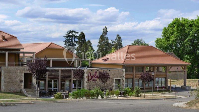 Bâtiment moderne avec toits en tuiles rouges, entouré d'arbres et d'une terrasse avec tables et chaises.