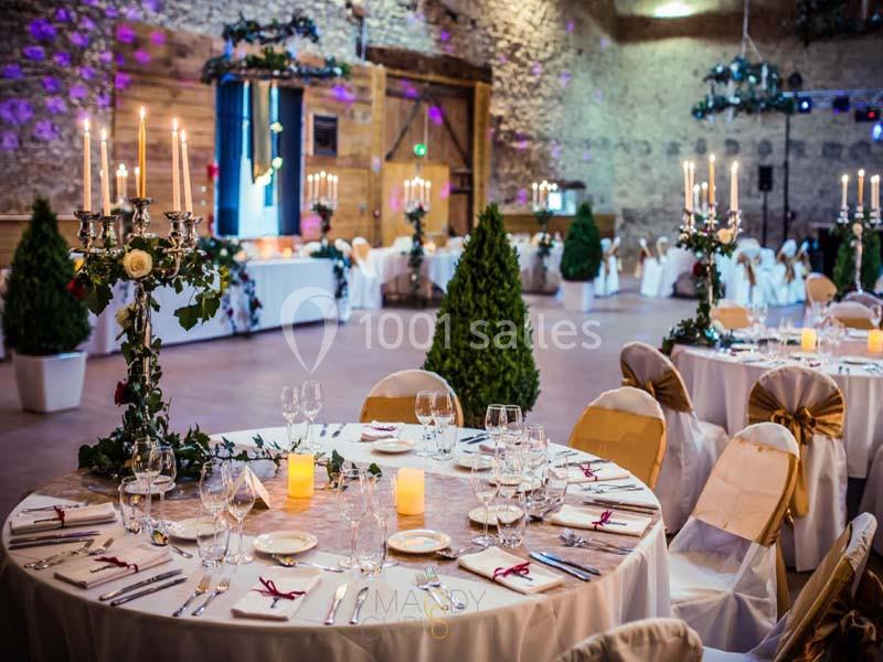 Salle de réception décorée pour un mariage, avec tables dressées, chandeliers, bougies et plantes en pot.