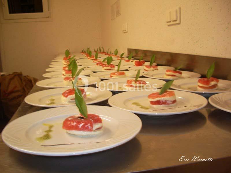 Assiettes alignées contenant des entrées de tomates, mozzarella et feuilles de basilic, avec un filet de sauce verte.