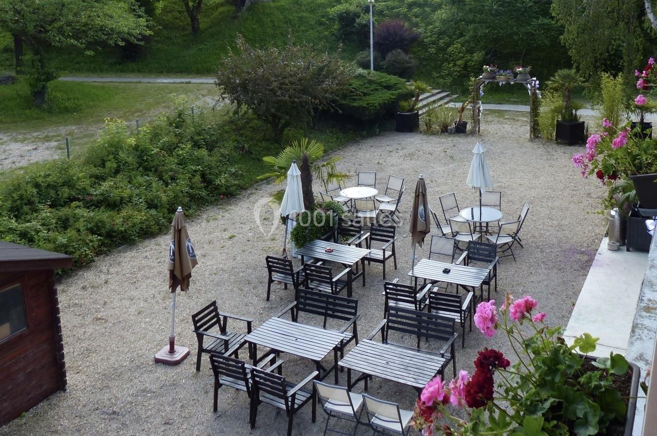 Terrasse extérieure avec tables et chaises en métal, entourée de verdure et décorée de fleurs.