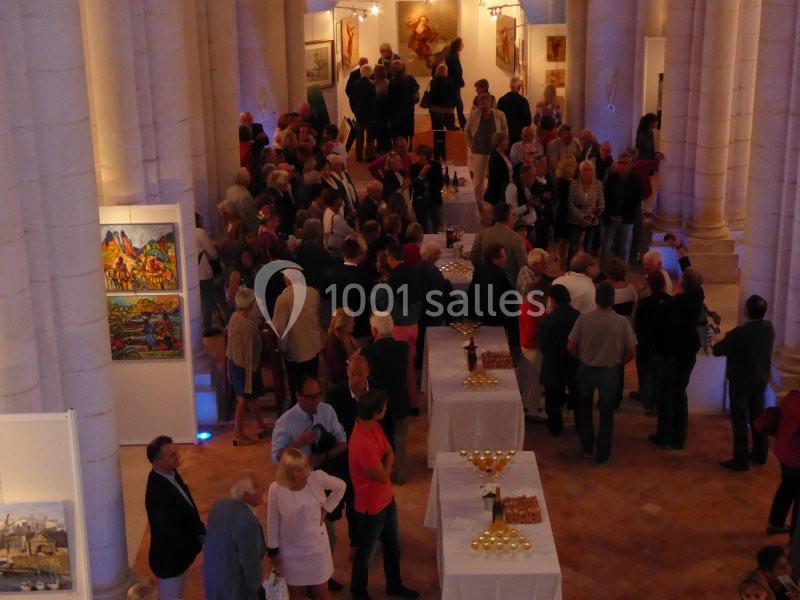 Groupe de personnes rassemblées dans une salle voûtée pour un événement, entourées de peintures exposées.