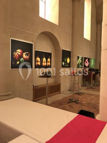 Exposition de photographies de légumes colorés accrochées sur les murs d'un espace intérieur aux colonnes en pierre.