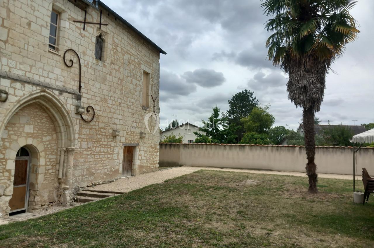 Vue d'un bâtiment en pierre ancienne avec une arche, un palmier et une pelouse sous un ciel nuageux.