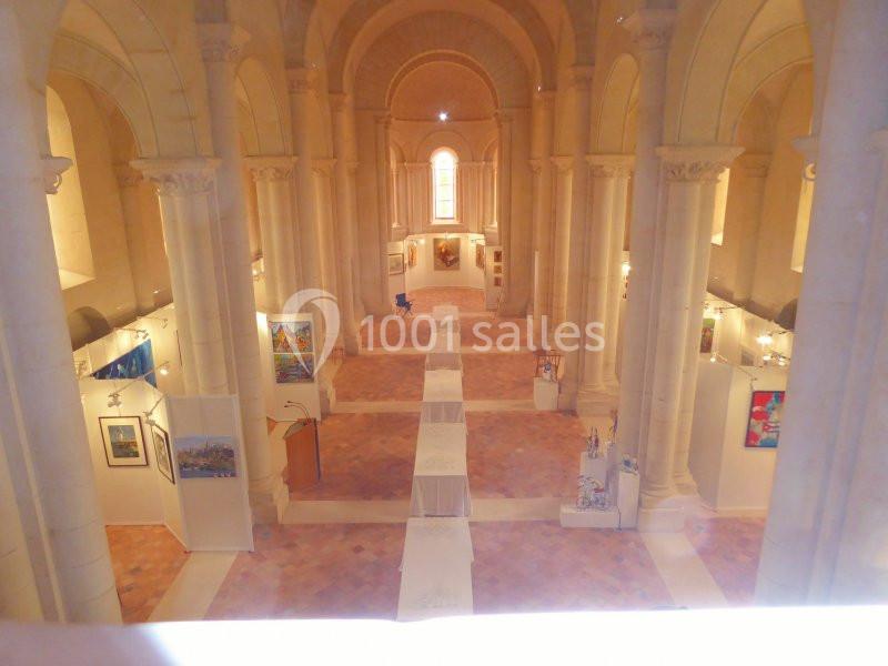 Vue intérieure d'une église transformée en espace d'exposition avec des œuvres d'art accrochées le long des murs.