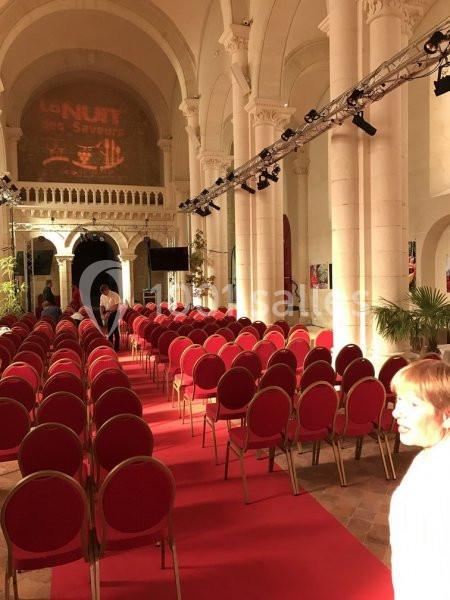Rangées de chaises rouges alignées sur un tapis rouge dans une salle voûtée avec éclairage et décorations.