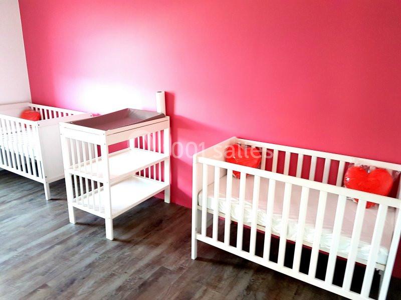 Deux lits pour bébé blancs et une table à langer dans une pièce aux murs roses et au sol en parquet.