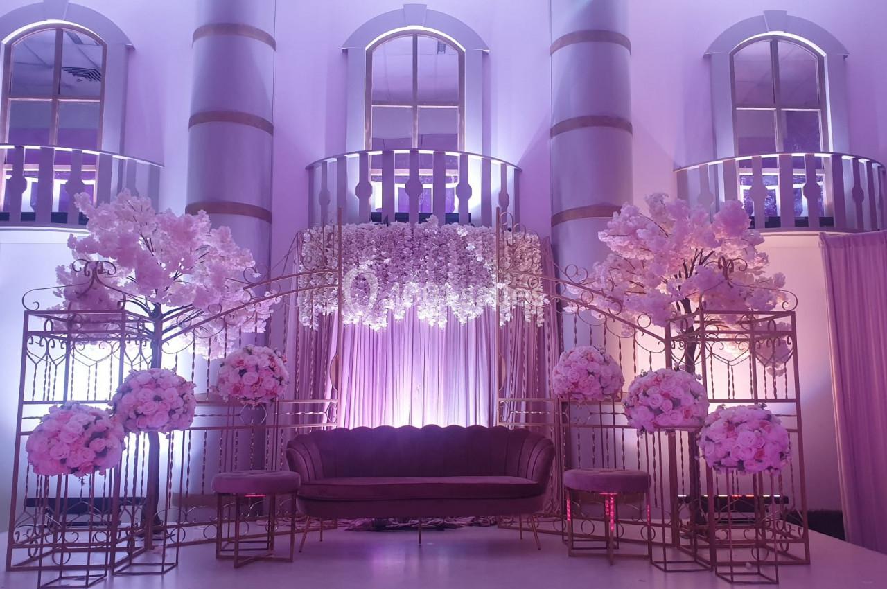 Décor intérieur élégant avec un canapé rose, des arches fleuries et des colonnes éclairées par une lumière violette.
