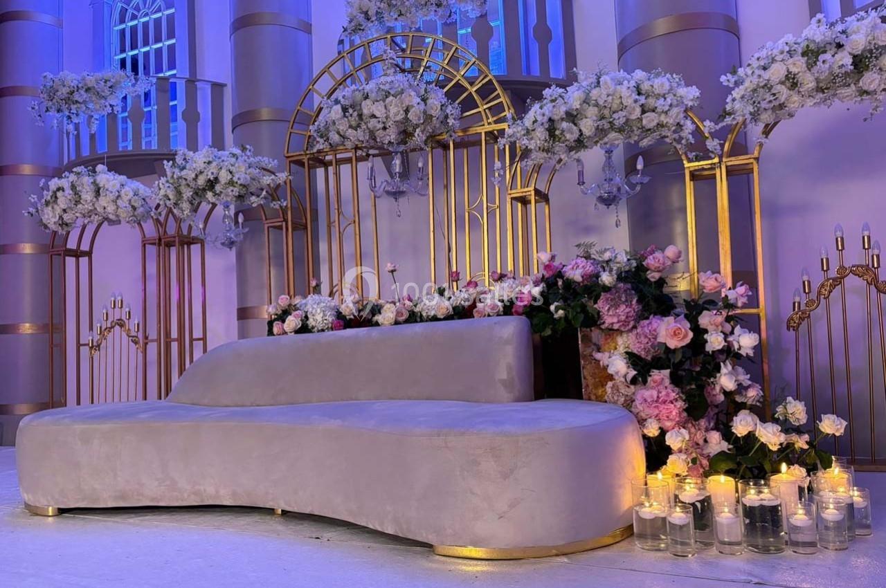Décor élégant avec canapé gris, arches dorées, fleurs blanches et roses, et bougies dans un cadre lumineux.