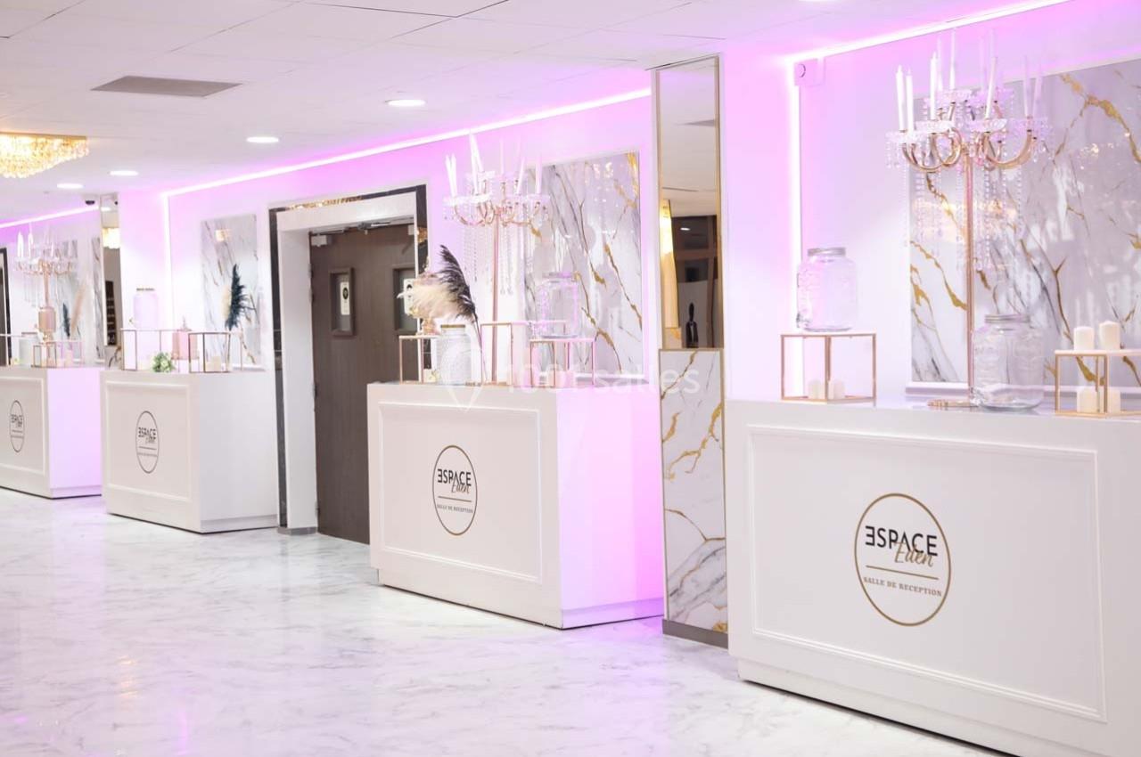 Salle de réception lumineuse avec comptoirs blancs, décorations élégantes et éclairage rose.