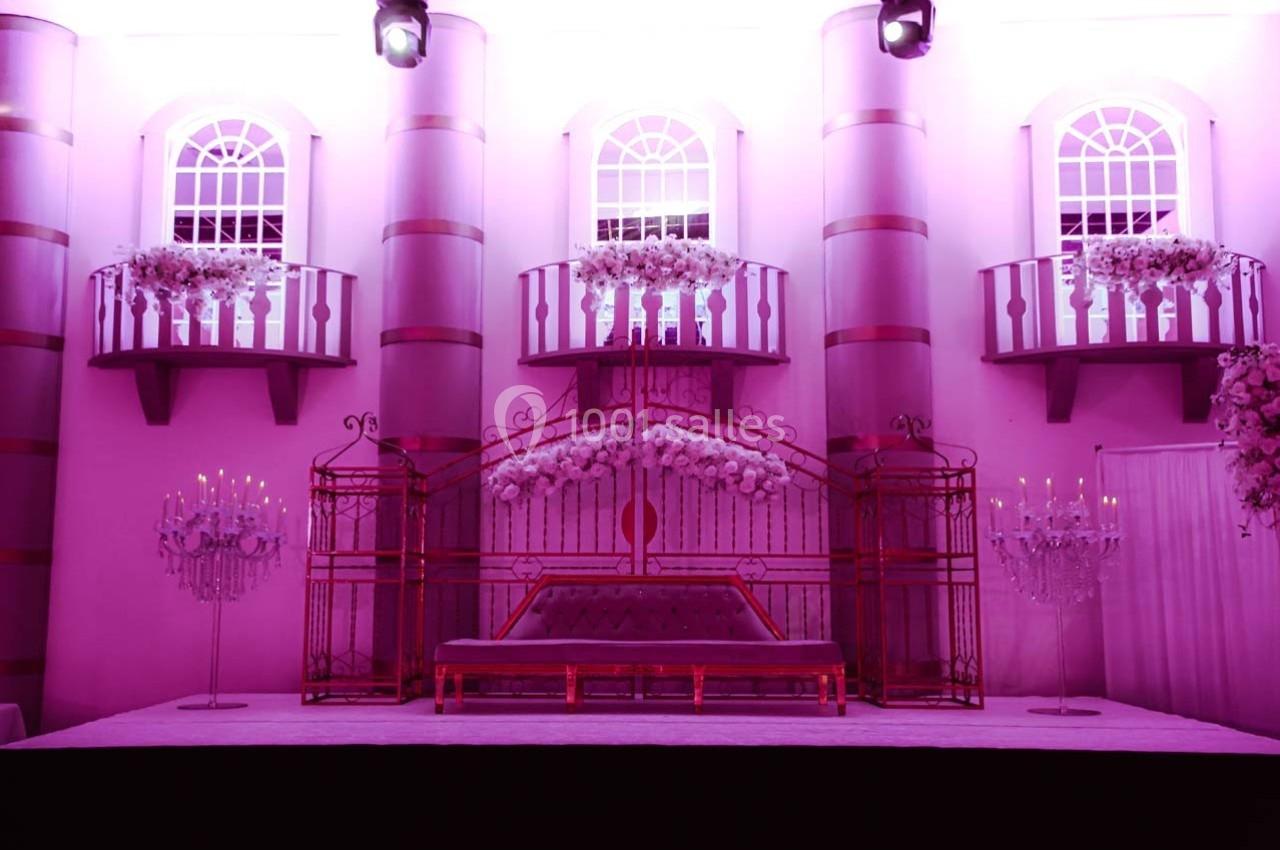 Décor intérieur avec une scène ornée de fleurs, un canapé central et des balcons illuminés en arrière-plan.