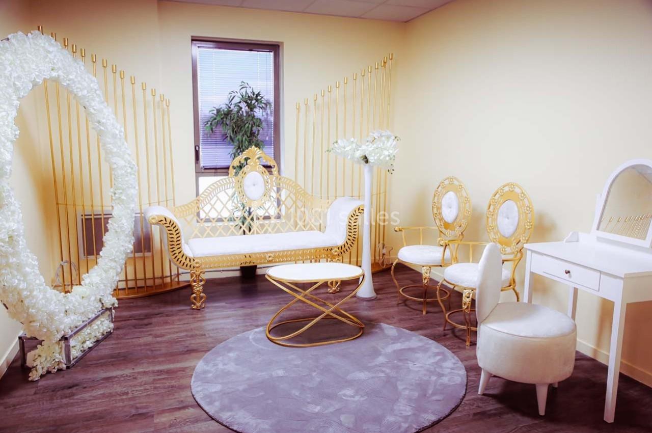 Salle lumineuse avec mobilier doré et blanc, comprenant un canapé, des chaises, une coiffeuse et un décor floral.