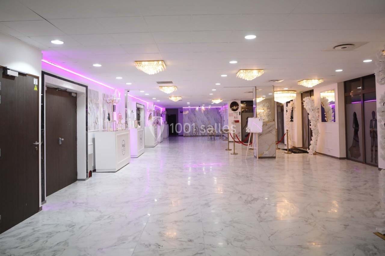 Salle spacieuse avec sol en marbre, éclairage rose, lustres et décorations élégantes, portes et comptoirs visibles.