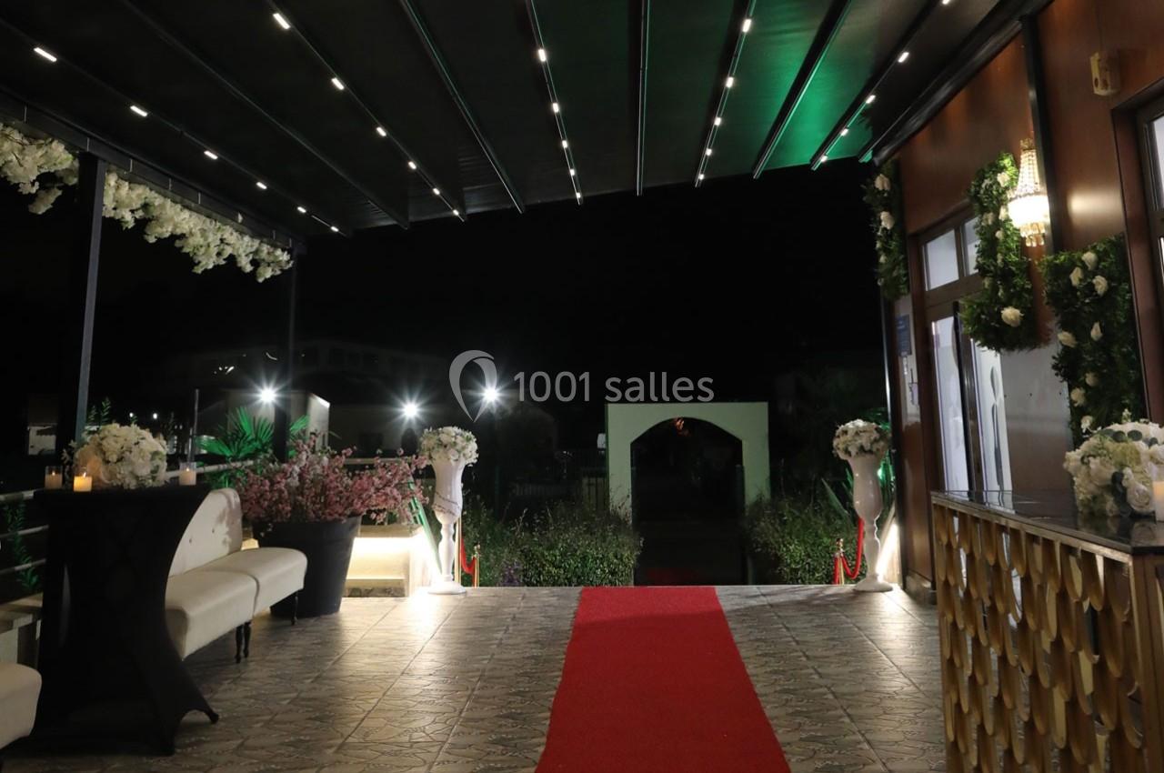 Entrée décorée avec tapis rouge, fleurs et éclairage nocturne sous une pergola.