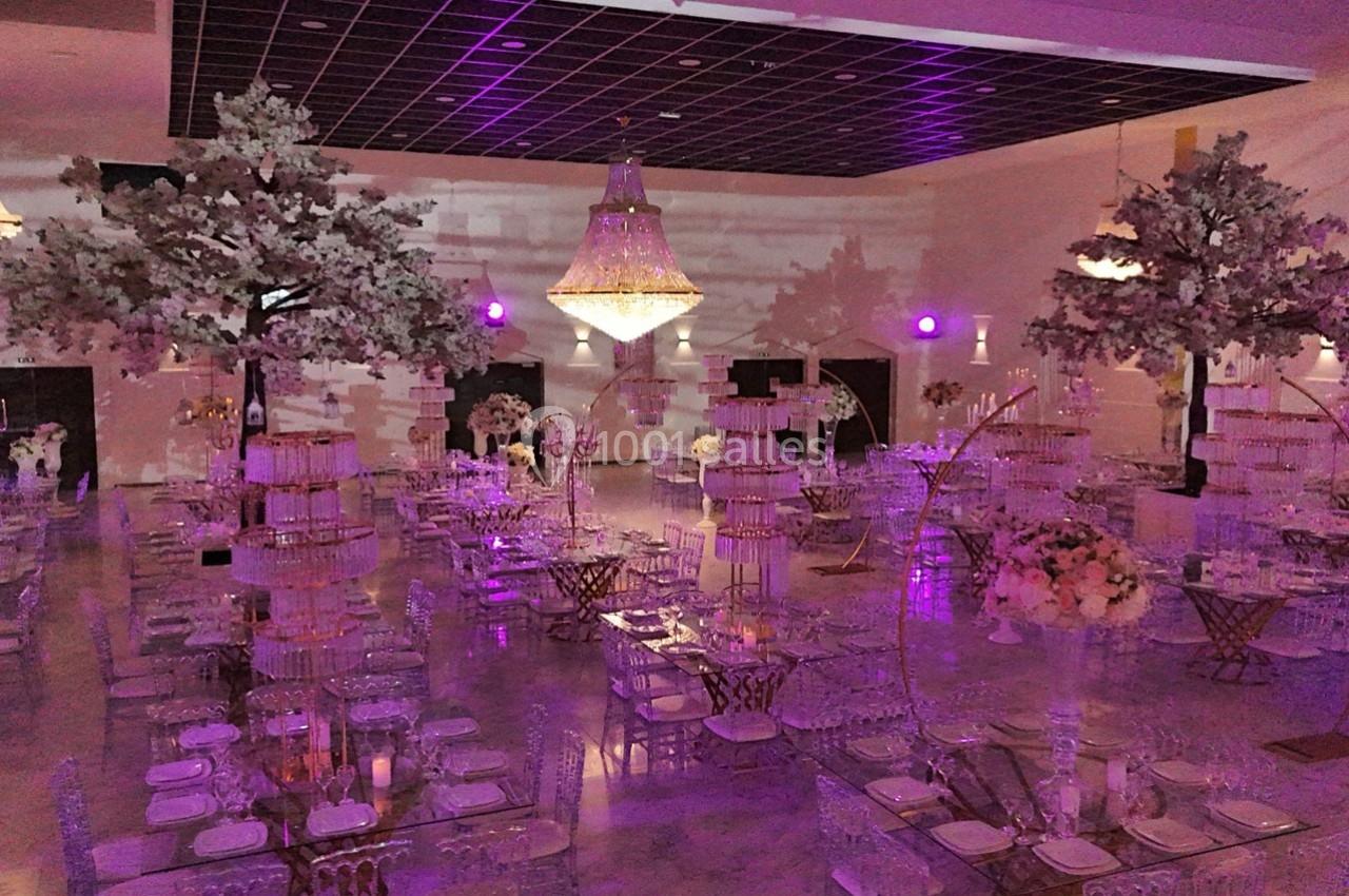 Salle de réception décorée avec des tables élégantes, des arbres artificiels et un éclairage violet tamisé.