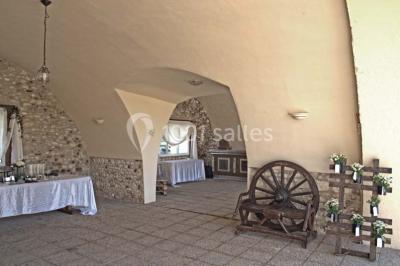 Salle de réception en pierre décorée de ballons rouges et blancs, avec tables dressées pour un événement.