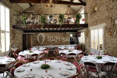 Salle de réception en pierre décorée de ballons rouges et blancs, avec tables dressées pour un événement.