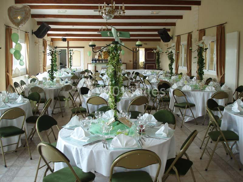 Salle de réception décorée avec des tables rondes, nappes blanches, chaises vertes et colonnes ornées de feuillage.