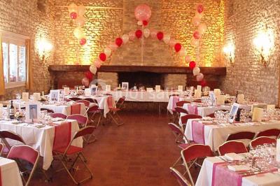 Salle de réception en pierre décorée de ballons rouges et blancs, avec tables dressées pour un événement.