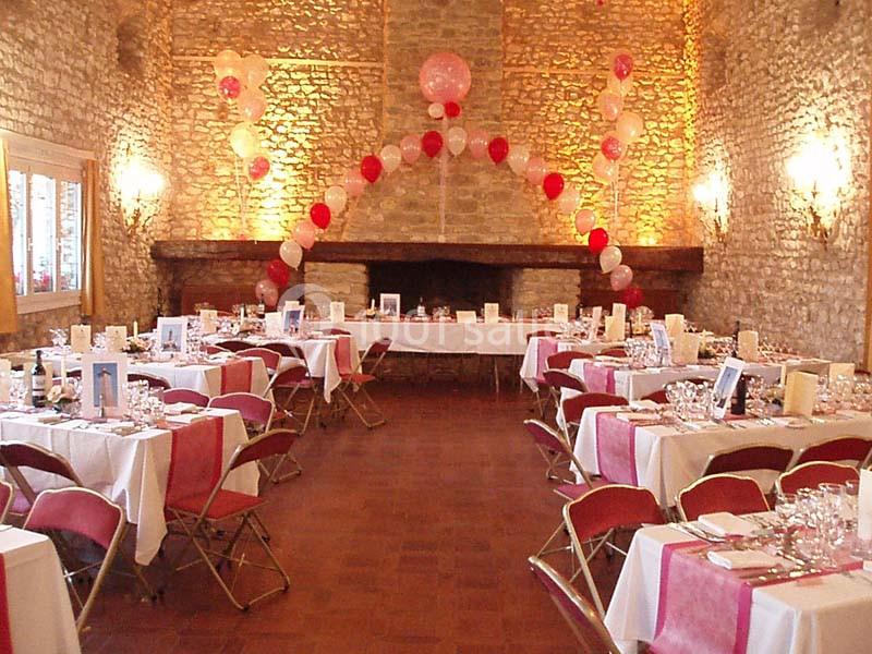 Salle de réception en pierre décorée de ballons rouges et blancs, avec tables dressées pour un événement.