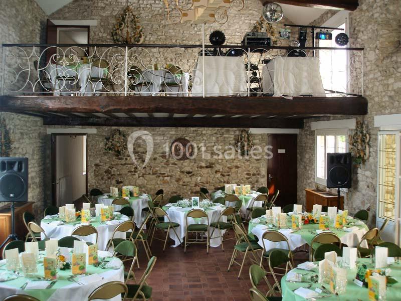 Salle en pierre avec mezzanine, tables rondes dressées pour un événement, décorations florales et équipements audio visibles.