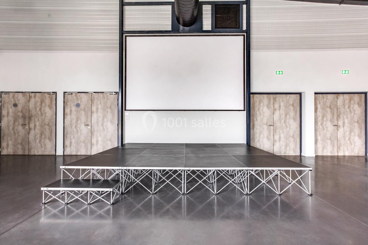 Estrade métallique avec une petite marche, placée dans une salle moderne avec un écran blanc et des portes en bois.