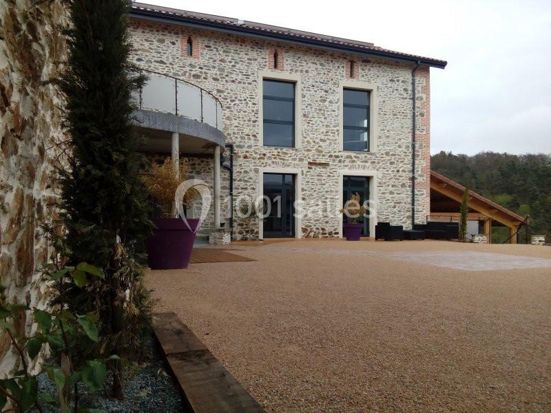 Façade en pierre d'une maison rénovée avec terrasse, grandes fenêtres et espace extérieur gravillonné.