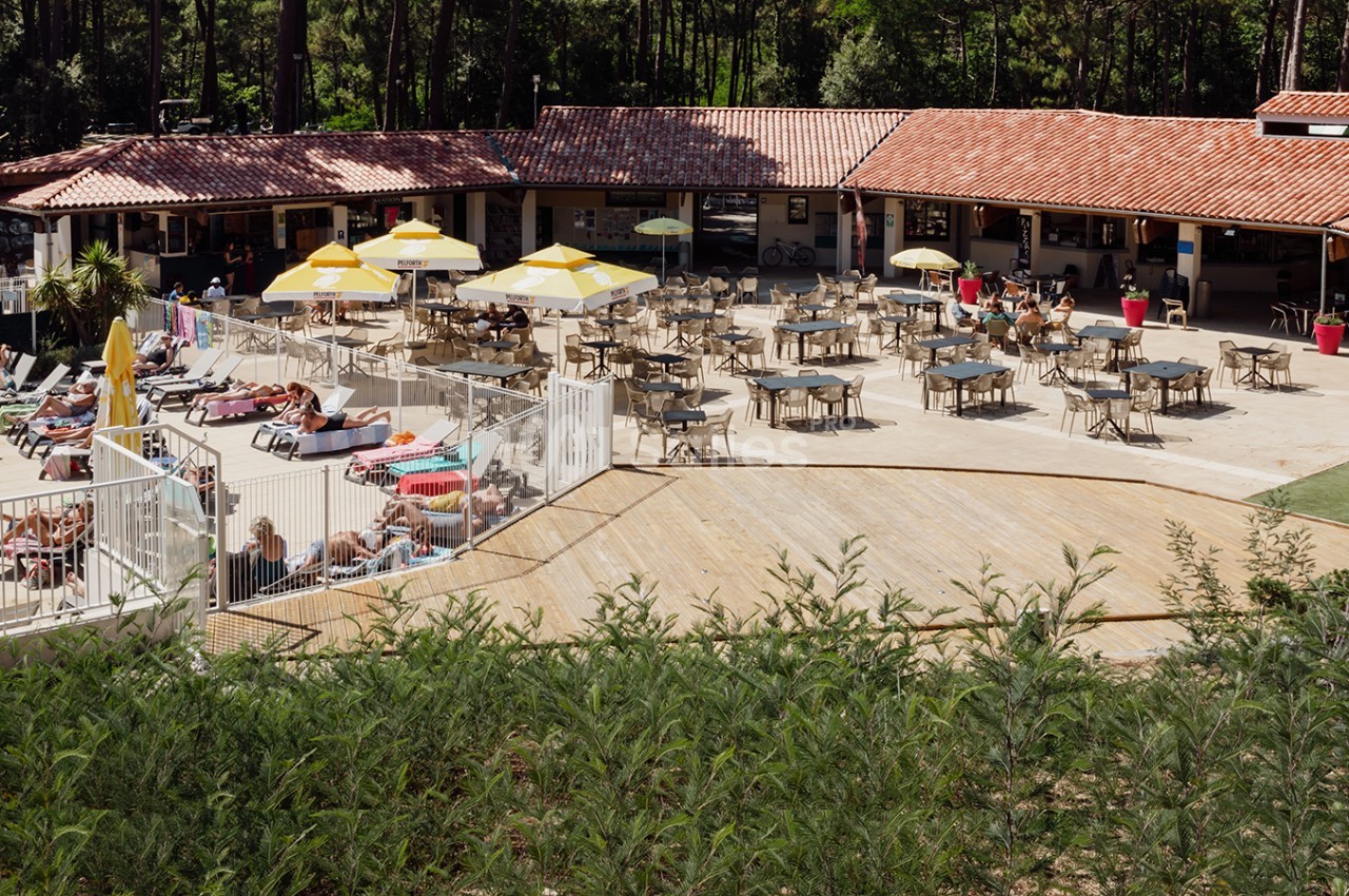 Terrasse d'un restaurant avec tables, chaises et parasols jaunes, près d'une piscine entourée de végétation et de transats.