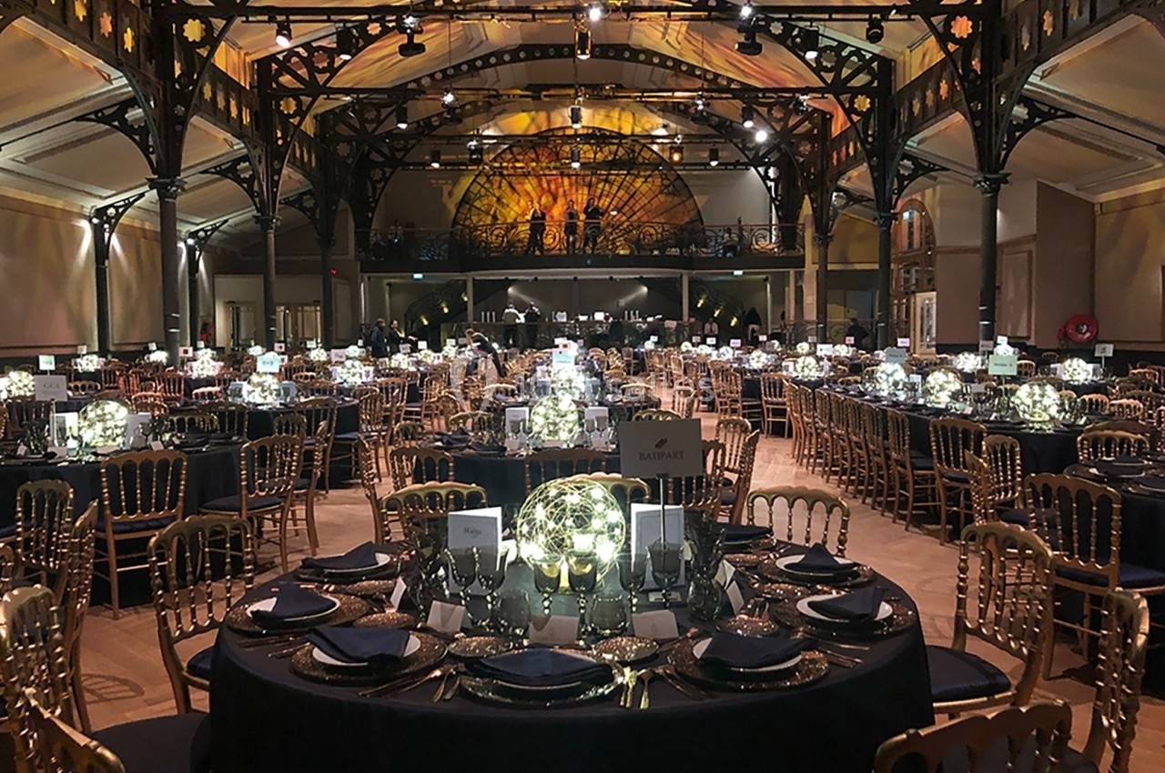 Salle de réception élégante avec tables rondes dressées, décorations lumineuses et éclairage chaleureux.