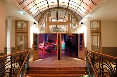 Salle intérieure avec mezzanine, escaliers symétriques, balustrades en métal décoratif et parquet au sol.