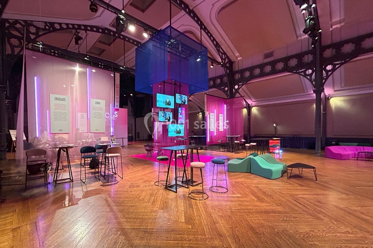 Salle spacieuse avec parquet, mobilier moderne et éclairage coloré, utilisée pour un événement ou une exposition.
