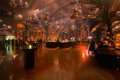 Salle intérieure avec mezzanine, escaliers symétriques, balustrades en métal décoratif et parquet au sol.