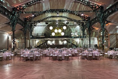 Salle intérieure avec mezzanine, escaliers symétriques, balustrades en métal décoratif et parquet au sol.