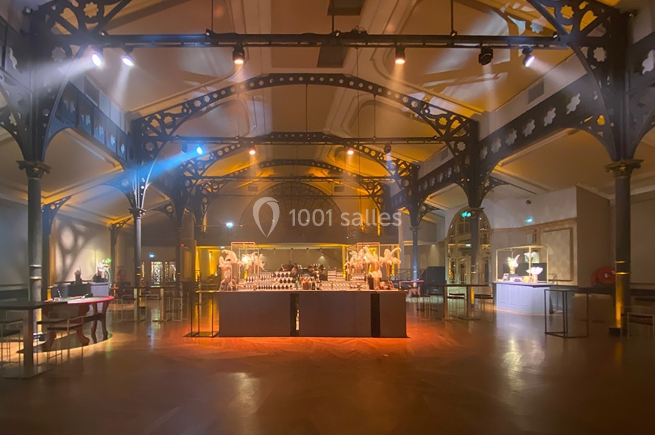 Salle lumineuse avec structure métallique, parquet en bois et tables disposées pour un événement ou une réception.