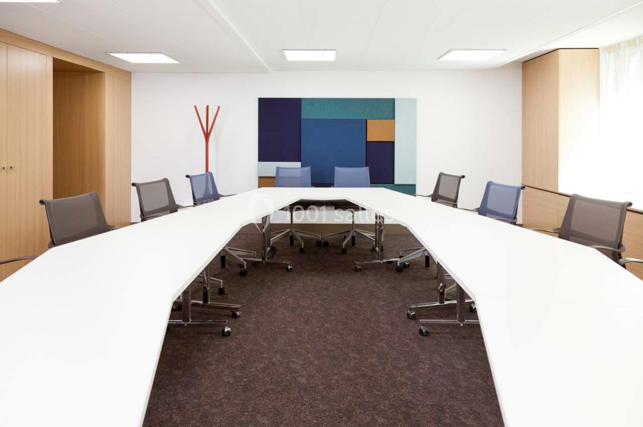 Salle de réunion moderne avec une grande table en U, chaises pivotantes et un mur décoré de panneaux colorés.