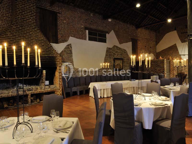 Salle de réception avec murs en briques, tables rondes dressées et chandeliers allumés dans une ambiance chaleureuse.