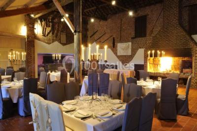 Miniature Location salle Pont-à-Celles (Hainaut) - La Ferme de la Pitance #6 Salle de réception avec tables dressées, nappes beiges, chandeliers et poutres apparentes sous un toit vitré.