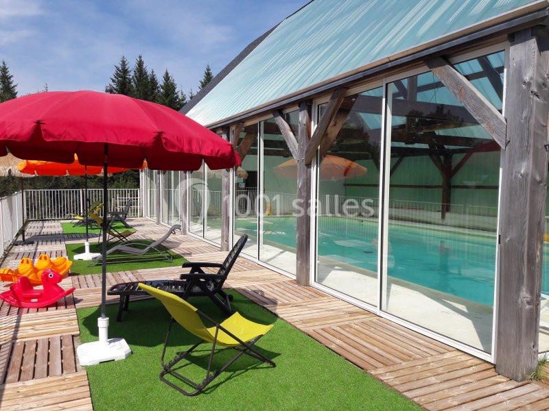 Terrasse avec chaises longues, parasols colorés et vue sur une piscine intérieure entourée de baies vitrées.